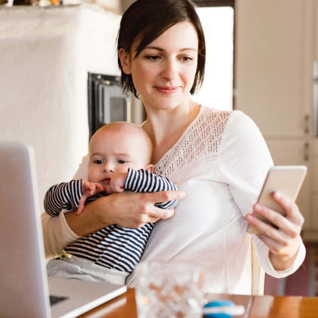 Lady holding a baby and viewing an app on her mobile phone